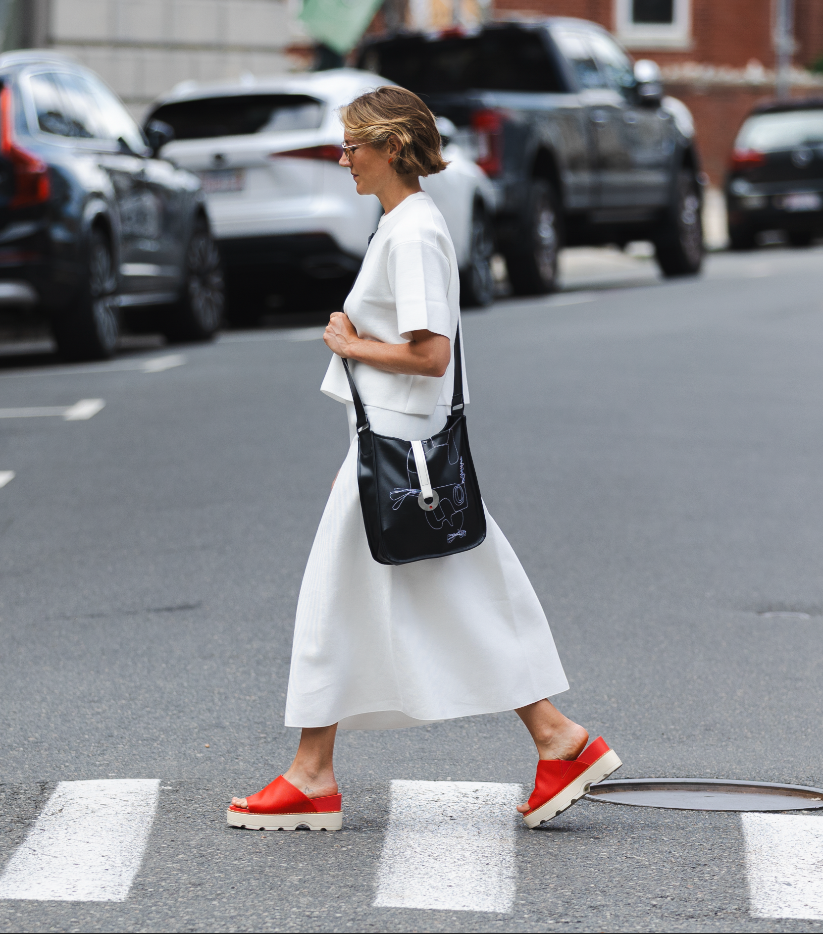 Woman in a white dress with red shoes walking on a street.