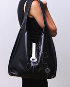 Woman holding a black bag with a unique design on a plain background