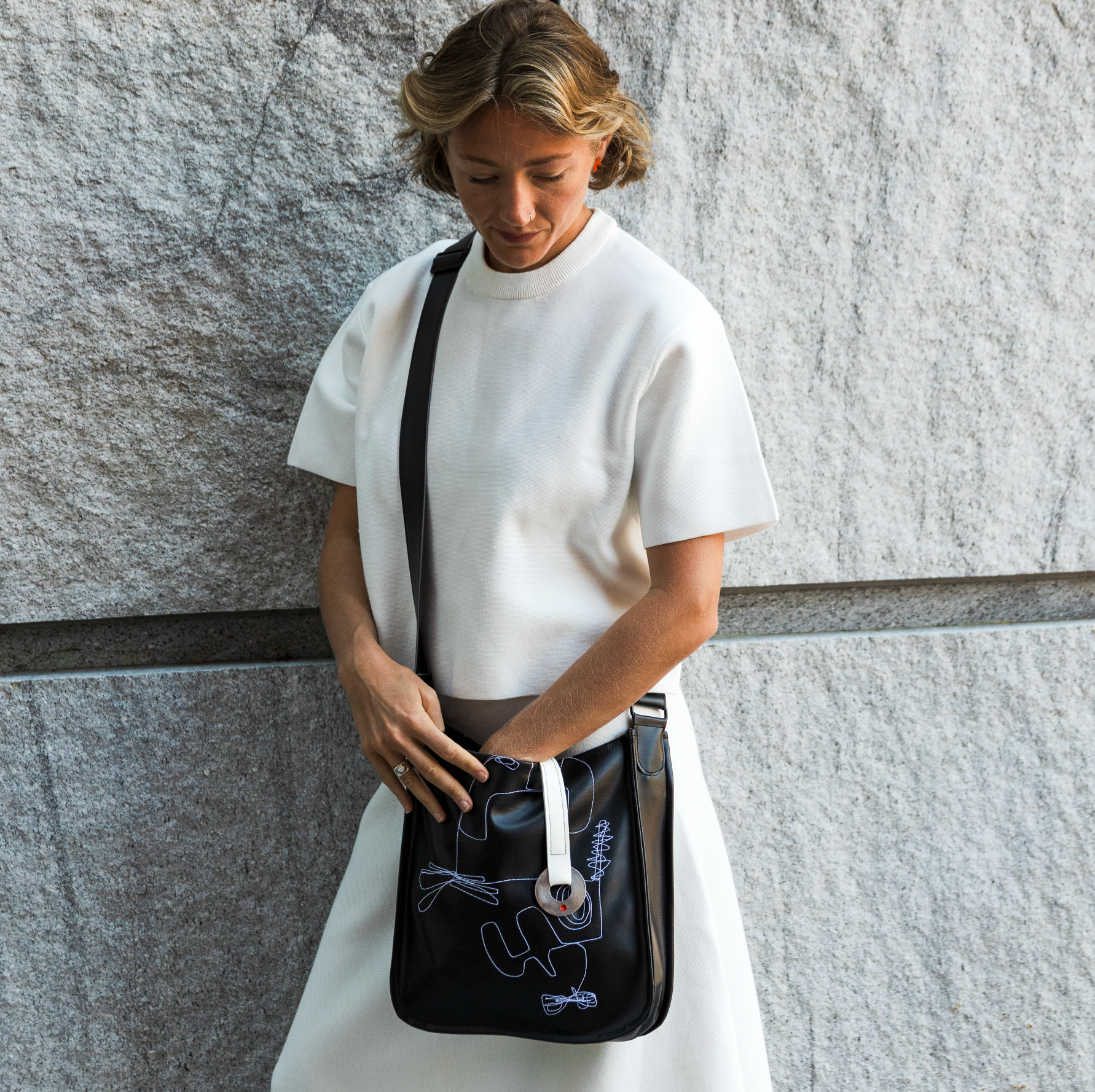 Person holding a black bag with white strap against a gray wall