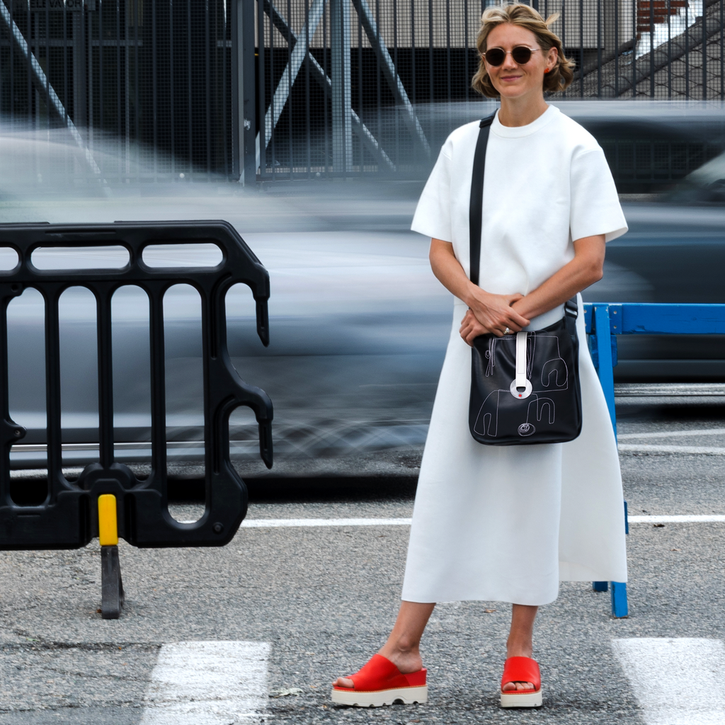 Woman in a white outfit with a black bag standing on a street.