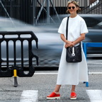 Woman in a white outfit with a black bag standing on a street.