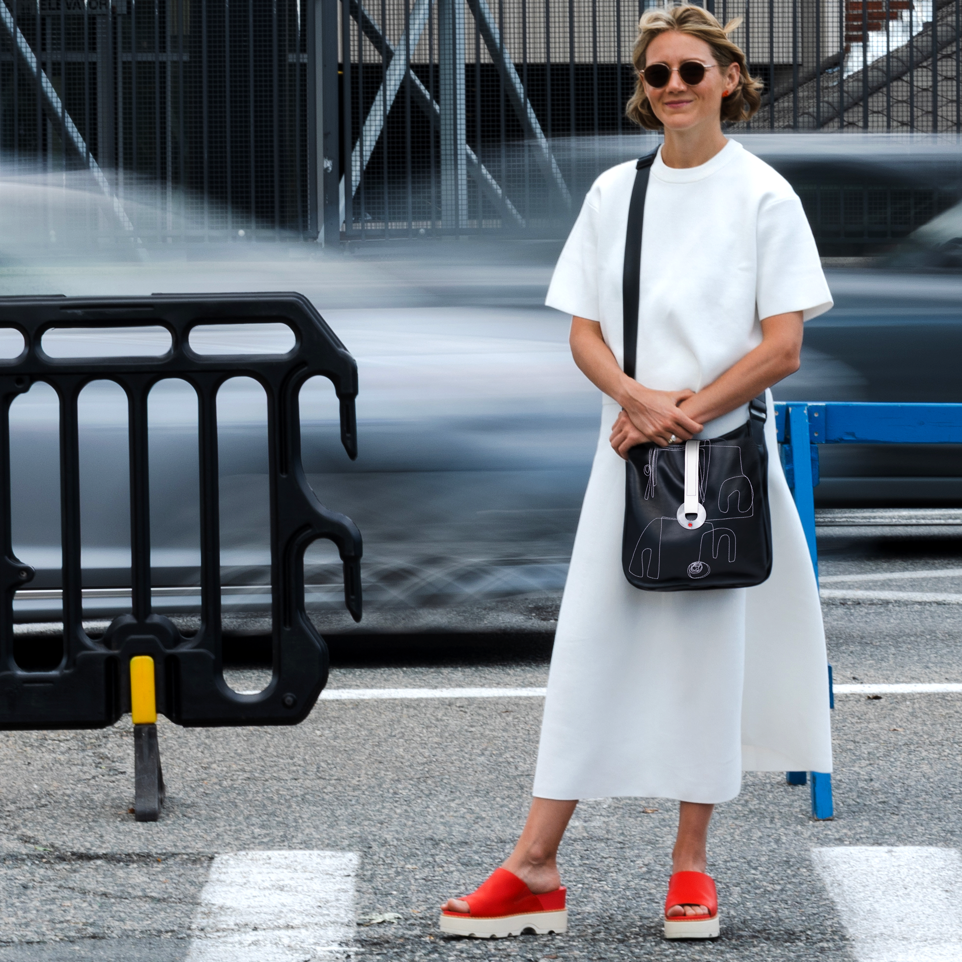 Woman in a white outfit with a black bag standing on a street.